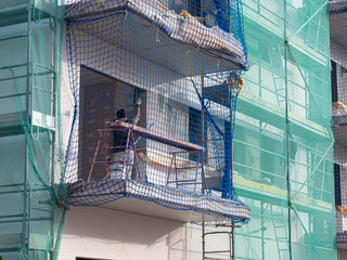 Persona trabajando en la construcción de un edificio pintando una pared, con redes de protección...