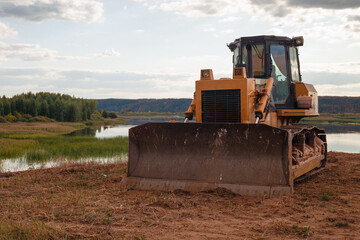 crawler tractor with bucket stands on the background of forest lake