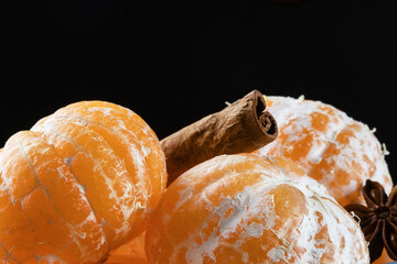 peeled tangerines with tube of cinnamon and star anise on dark background, close-up