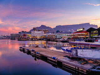Naklejka premium Victoria and Alfred, V and A waterfront lit up during a colorful sunset with table mountain in the background, Cape Town, South Africa
