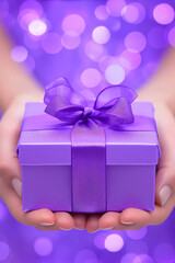 Purple gift box with ribbon in women's hands.