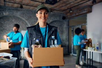 Happy female charity worker with donation box at food bank looking at camera.