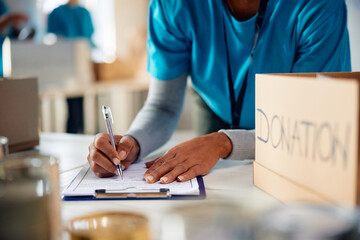 Close up of black woman writing list of donations while volunteering at community center.