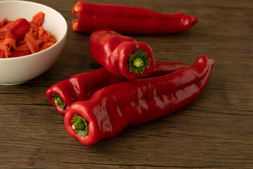 fresh red peppers on wooden board with white bowl with already roasted peppers