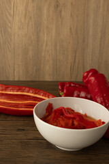 fresh red peppers on wooden board with white bowl with already roasted peppers
