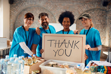 Multiracial group of volunteers holding placard with 'Thank you' message while working at...