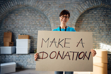 Happy female volunteer with 'make a donation' placard looking at camera.