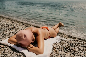 A woman sunbathes on the beach, lying on her stomach in a red swimsuit against the sea backdrop.
