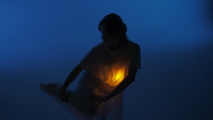 Female dancer performing in the studio. Young woman dancing in dark studio with warm light glowing inside the chest under her shirt.