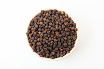 Dry black pepper spice in bowl on a white background.
