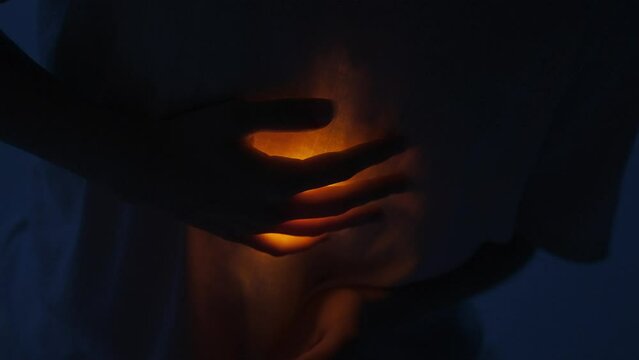 Female dancer performing in the studio. Young woman in dark studio touching warm light glowing inside the chest under her shirt, close up. 60 fps