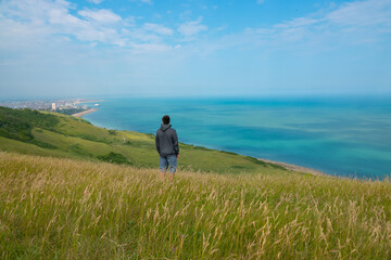 Young man admires beautiful coastal landscape from a viewpoint on top of a cliff