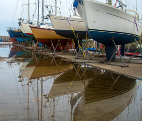 Boats out of the water on a marina with colourful reflection in puddles after the rain