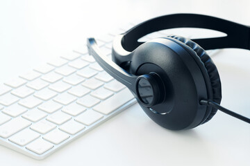 Headset with microphone and keyboard, placed on a white desk. Close-up view. Remote work or...