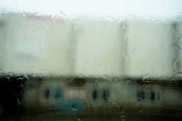 Abstraktes Motiv mit Regentropfenmuster auf Glasscheibe vor Industriegebäude mit Fensterfront und Flachdach bei Regen am Morgen im Winter