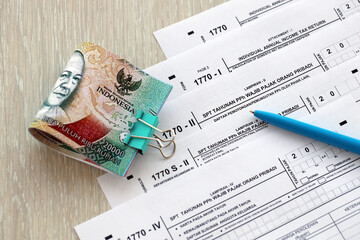 Annual Individual Income Tax Return forms with pen and indonesian rupiah bills. Original name is Surat Pemberitahuan Pajak or SPT Tahunan
