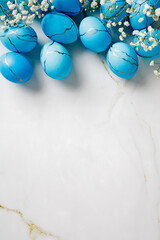 Vertical flat lay composition with painted blue Easter eggs and flowers on marble table. Top view.