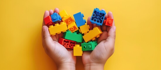 Hands holding colorful toy plastic bricks, blocks for building toys on yellow background - obrazy, fototapety, plakaty