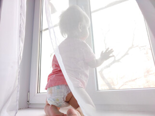 baby one year old stands on the windowsill, baby on the windowsill, trying to pull the window handle. Safety of children in the home