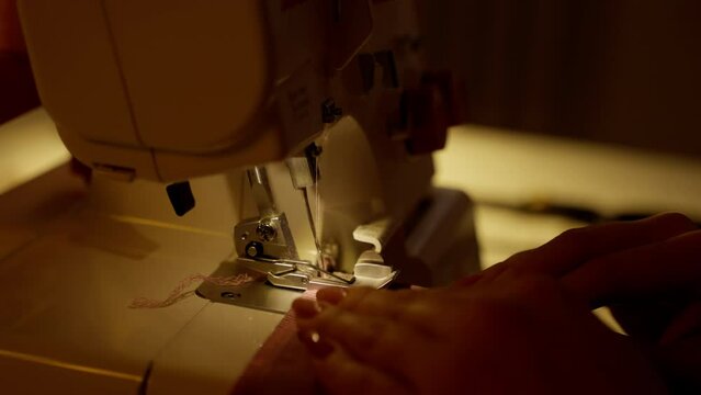 Hands Guiding Fabric Through Overlock Sewing Machine. Close-up of hands expertly guiding fabric through a serger for precise edging.