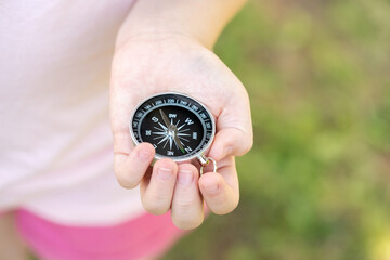 Close-up view of a child holding a black compass in hand blurred background, kids and outdoor navigation and exploration, discovery, career paths and jobs, education and development abstract concept