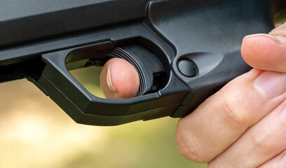 Detailed close-up of a persons index finger placed on the trigger of a black handgun, anonymous man ready to fire a simple sport firearm, air gun, firing a weapon. Gun safety rules, sports and weapons - obrazy, fototapety, plakaty