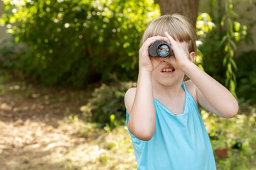 Young child uses binoculars to explore the garden, looking for something through the monocular, copy space searching, seeking, spying to find something. Curiosity and exploration simple concept
