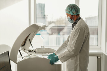 Male scientist in uniform and mask working in medical research laboratory use special equipment