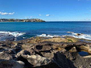 Fototapeta na wymiar Bay and coast of the ocean. View of the city in the distance. Turquoise waves breaking on the rocky shore. Australia, NSW, landscape.