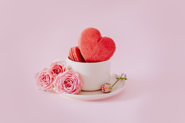 Pink heart shaped french macarons with rose flowers on a pink pastel background. Concept for Valentine's day.