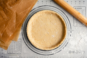 Unbaked Pastry Dough in a Tart Pan: Raw pie crust in a fluted pan on a floured work surface with a...