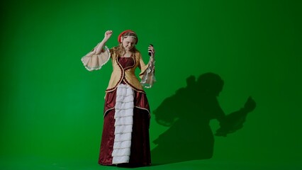 Woman in ancient outfit on chroma key green screen. Female in renaissance style dress in headphones listens music on smartphone and dancing.