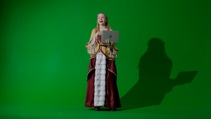 Woman in ancient outfit on chroma key green screen background. Female in renaissance style dress holding laptop typing message.