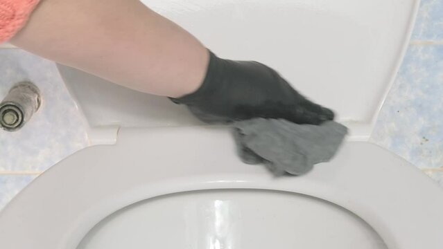 female hand in black latex glove carefully cleans dirty toilet with cloth, effectively care for bathroom and keep it clean, importance cleanliness for health