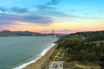 Fototapeta na wymiar aerial shot of the Golden Gate Bridge and the blue waters of the bay with lush green trees, plants and grass along the hillside and people on the beach in San Francisco California USA