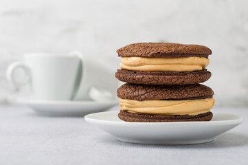 A stack of chocolate brownies on a plate and coffee cups on a light background. Horizontal.