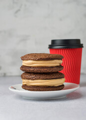 A stack of chocolate brownies on a plate and coffee in a red craft glass to go.