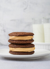 A stack of chocolate brownies on a plate and a glass of milk on a light background..