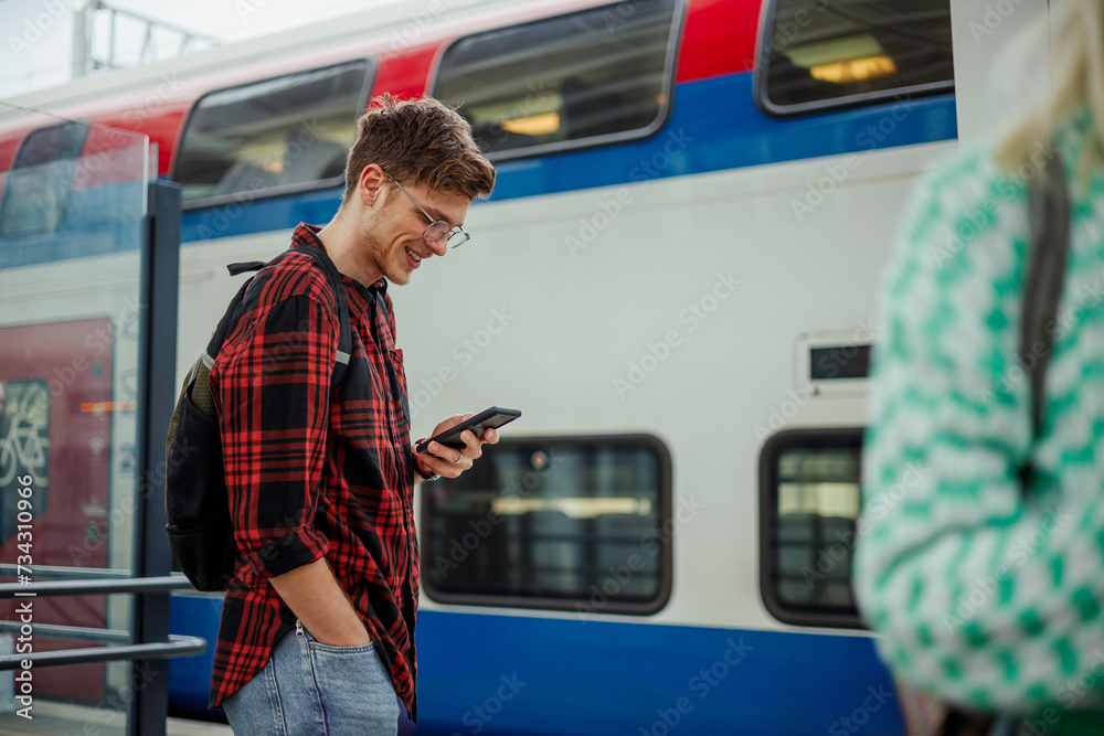 Wall mural Young man standing at the train station or a subway and using a phone