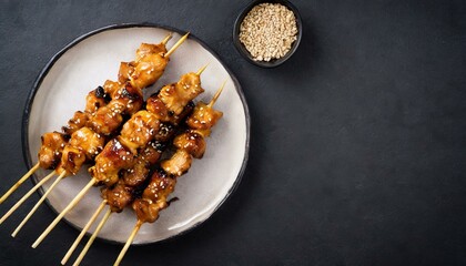Teriyaki chicken skewers on plate over black background with copy space. 