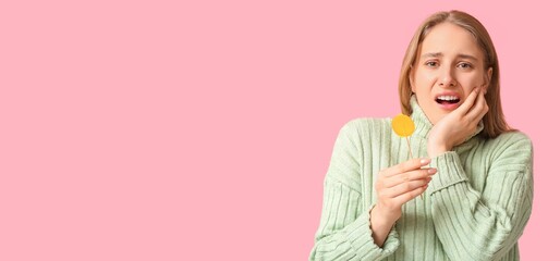 Young woman with lollipop feeling tooth ache on pink background with space for text