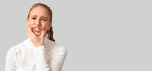 Young woman feeling tooth ache on light background with space for text