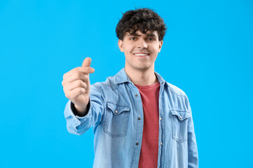 Handsome young man making heart with his fingers on light blue background