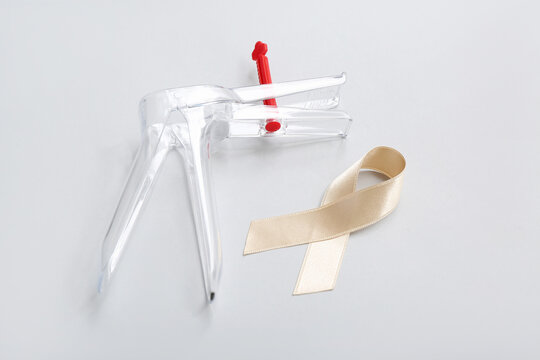 Beige ribbon with gynecological tool on light background. Uterine cancer awareness concept