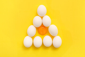 Triangle made of cracked and whole chicken eggs on yellow background