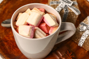 Cup of hot chocolate with marshmallows and gift boxes on table, closeup