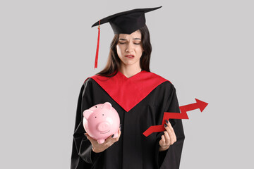 Sad female graduate student with piggy bank and arrow on light background. Price rise concept