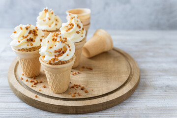 Cone cakes with cheese frosting and caramelized nuts on wooden board, ice cream alternative, party...