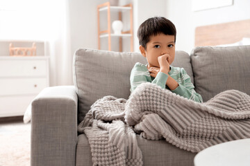 Ill little Asian boy coughing on sofa at home