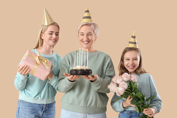 Little girl with her mom and grandmother celebrating Birthday on beige background